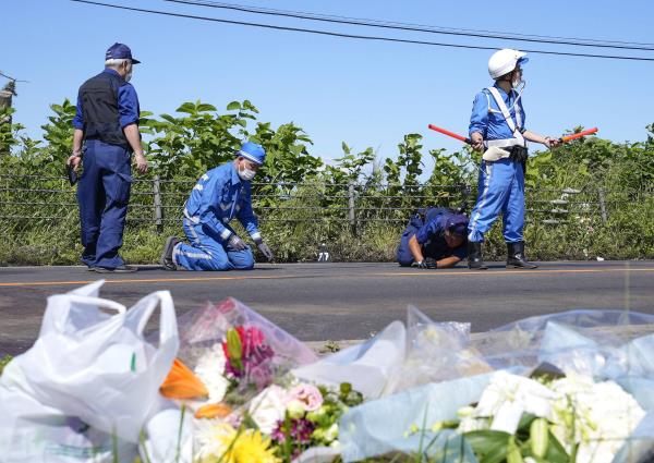 Flowers are laid near the site of a collision between a bus and a truck as investigators check the site in Yakumo, Hokkaido, on Monday. | KYODO