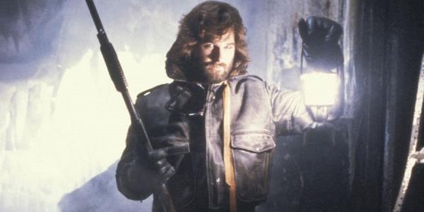 Kurt Russell In John Carpenter's The Thing holding a lantern and a weapon and standing in the snow